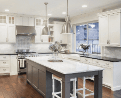 Modern kitchen with white cabinets, a gray island with a marble countertop, pendant lights, stainless steel appliances, and hardwood floors.